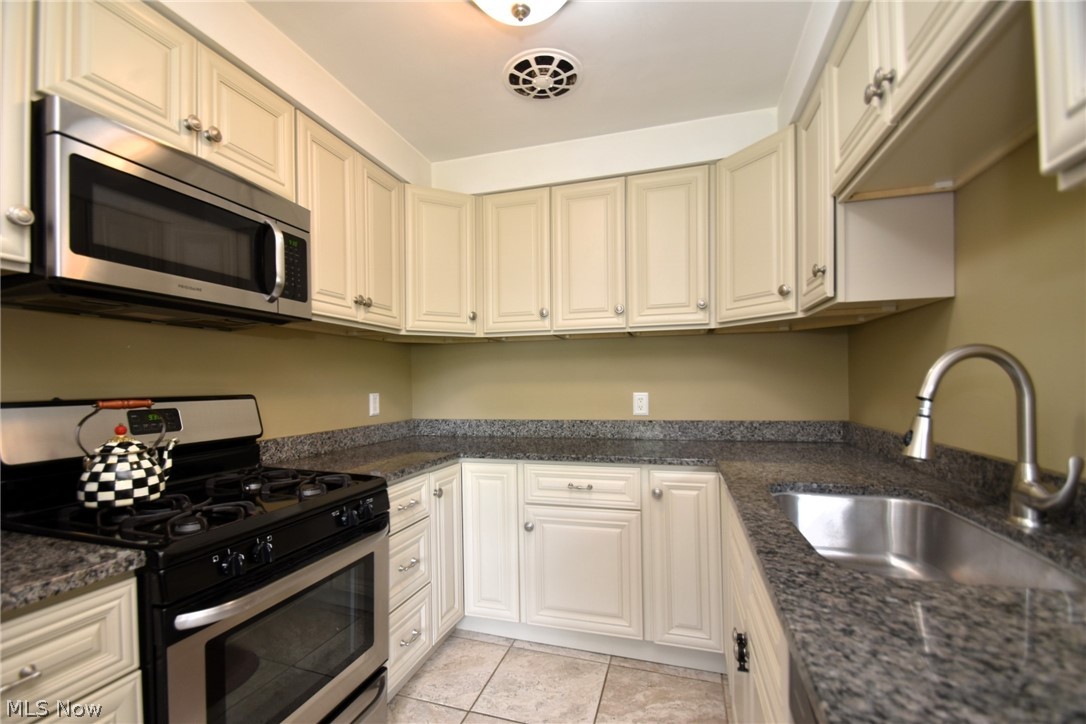 23901 Hazelmere Road Shaker Heights, OH 44122 - Photo 13 of 35 Kitchen featuring appliances with stainless steel finishes, sink, light tile floors, and dark stone countertops