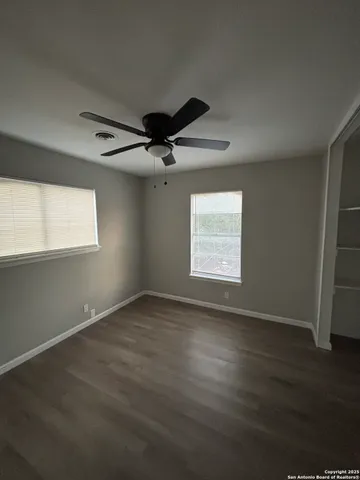 an empty room with wooden floor fan and windows