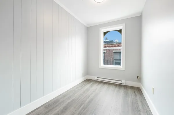 a view of an empty room with wooden floor and a window