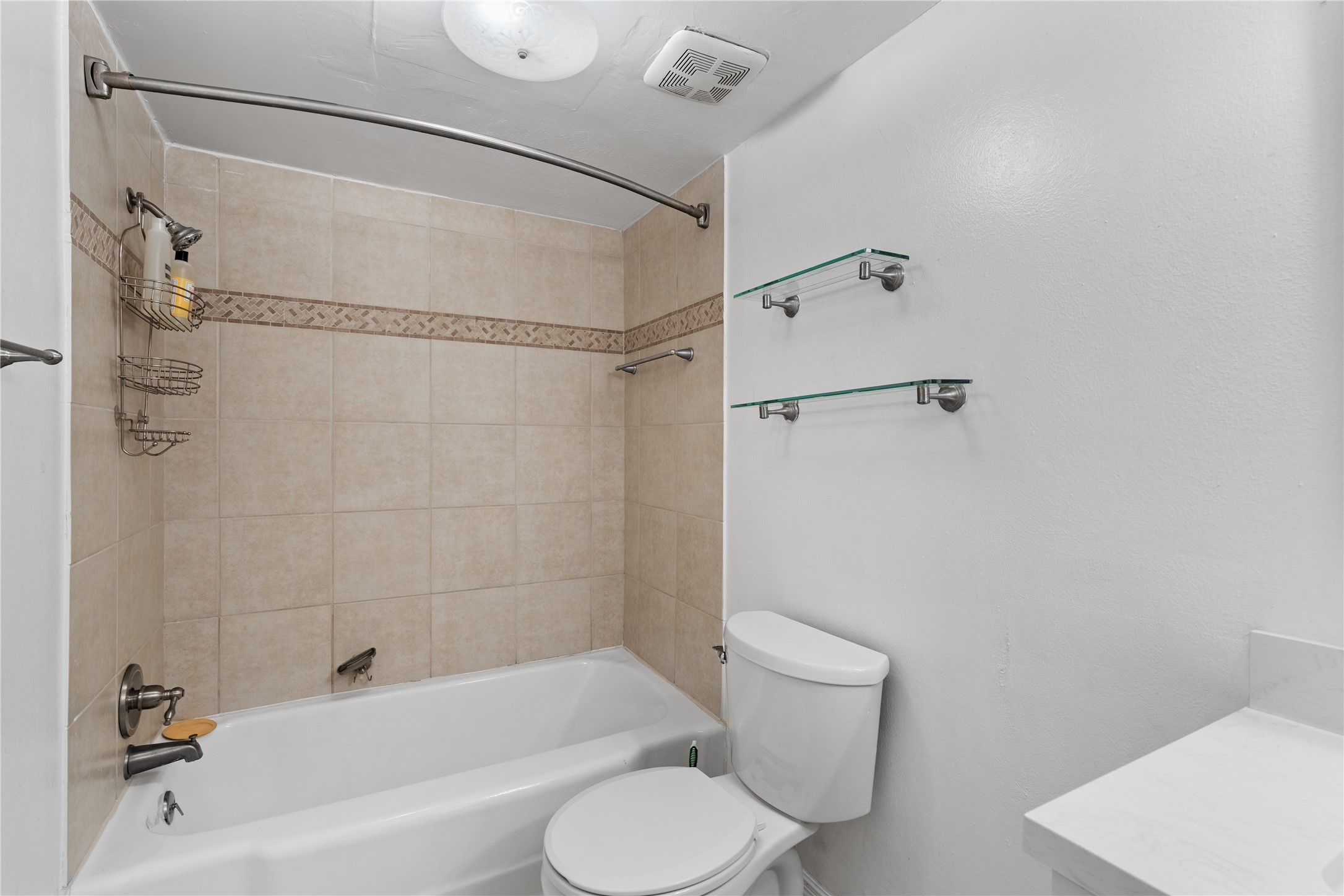 6303 Crab Orchard Road, Unit 3 Houston, TX 77057 - Photo 22 of 30 Relax in a full-sized tub surrounded by floor-to-ceiling porcelain tile in a warm, neutral sand tone. The custom decorative mosaic inlay adds a touch of artisan craftsmanship. Notice the sleek glass shelving—perfect for displaying your luxury spa products.