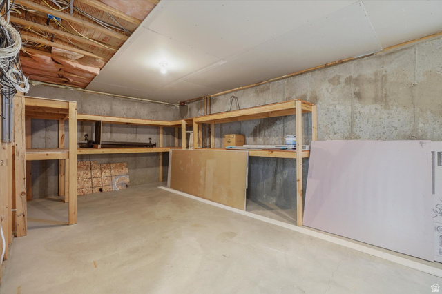 791 East Saddle Road Grantsville, UT 84029 - Photo 33 of 46 Unfinished basement space featuring exposed concrete walls, concrete flooring, and extensive built-in wooden shelving
