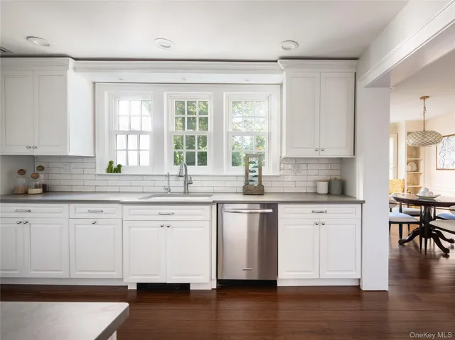 a kitchen with stainless steel appliances granite countertop a stove a sink and white cabinets with wooden floors