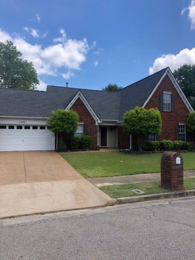 View of front of home featuring driveway, a front lawn, a shingled roof, brick siding, and a garage