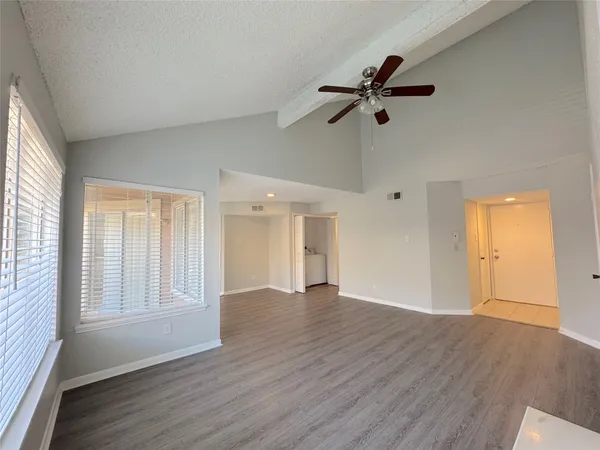 an empty room with wooden floor fan and windows