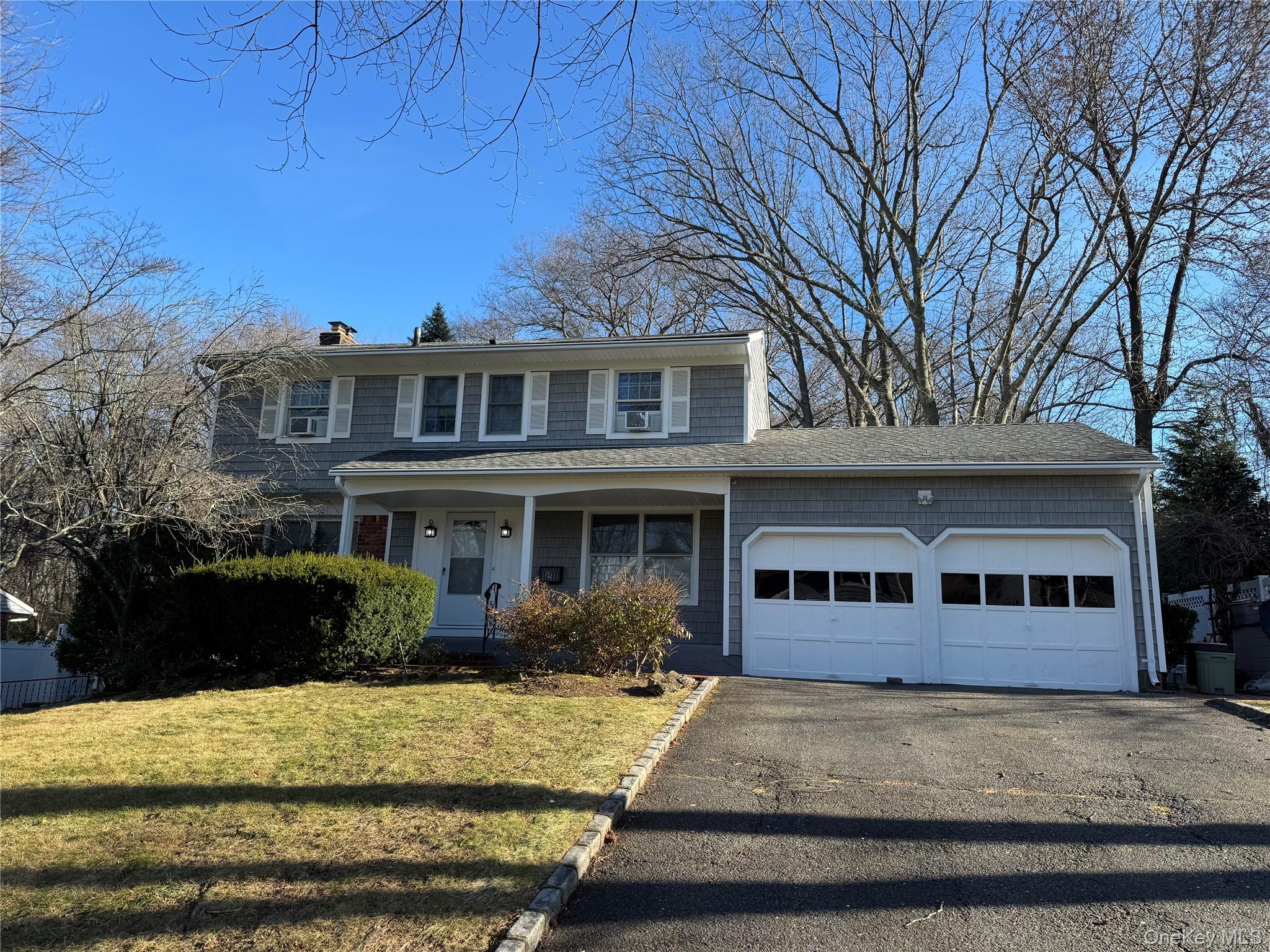Traditional-style home with a porch, a front yard, asphalt driveway, an attached garage, and a chimney