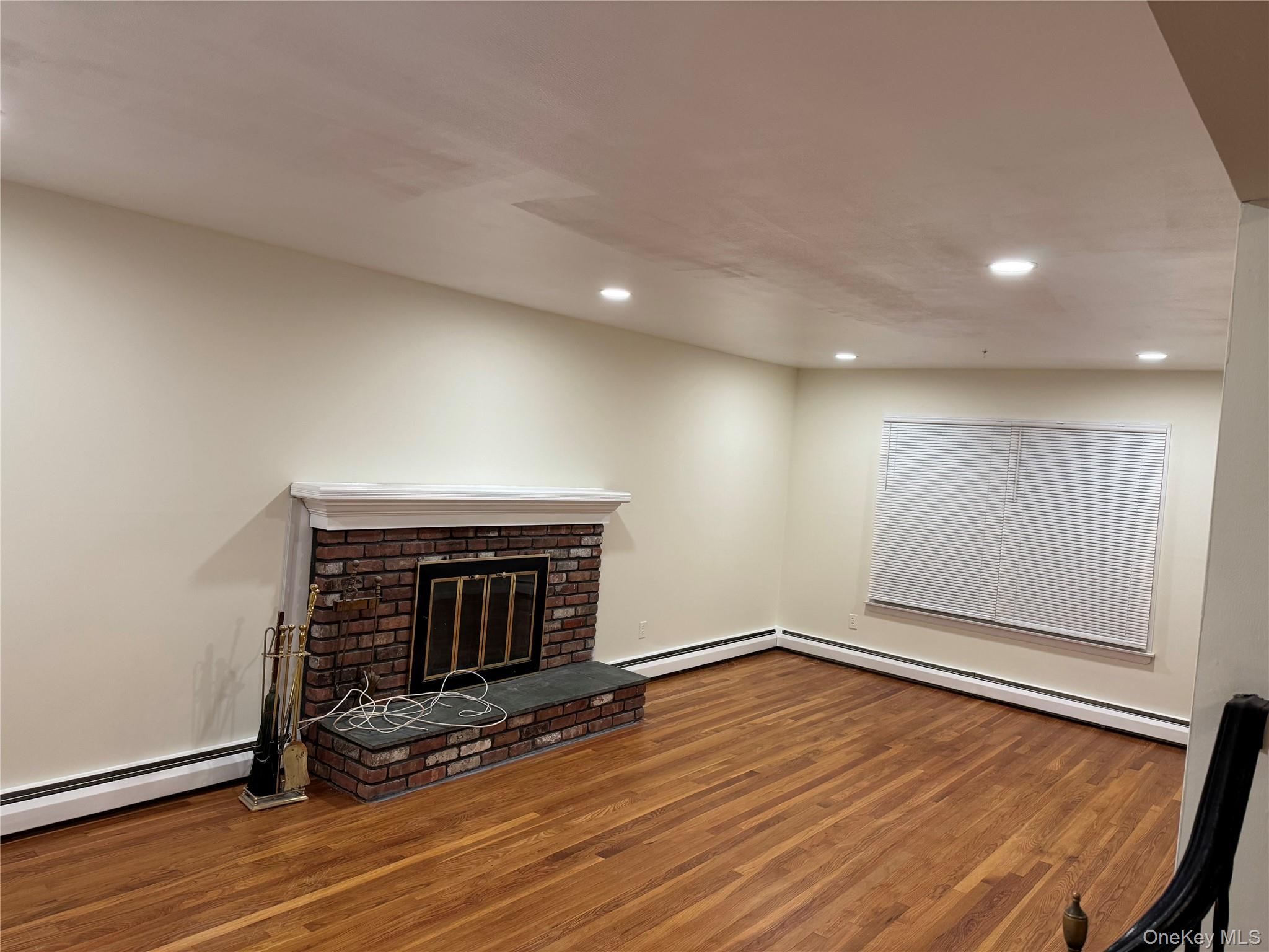 23 Jerome Road Syosset, NY 11791 - Photo 3 of 12 Unfurnished living room with a brick fireplace, recessed lighting, wood finished floors, a baseboard radiator, and a baseboard heating unit