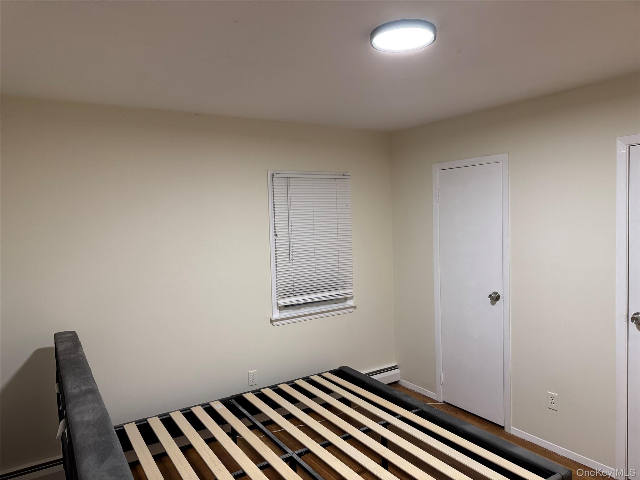 23 Jerome Road Syosset, NY 11791 - Photo 9 of 12 Unfurnished bedroom featuring a baseboard heating unit and wood finished floors