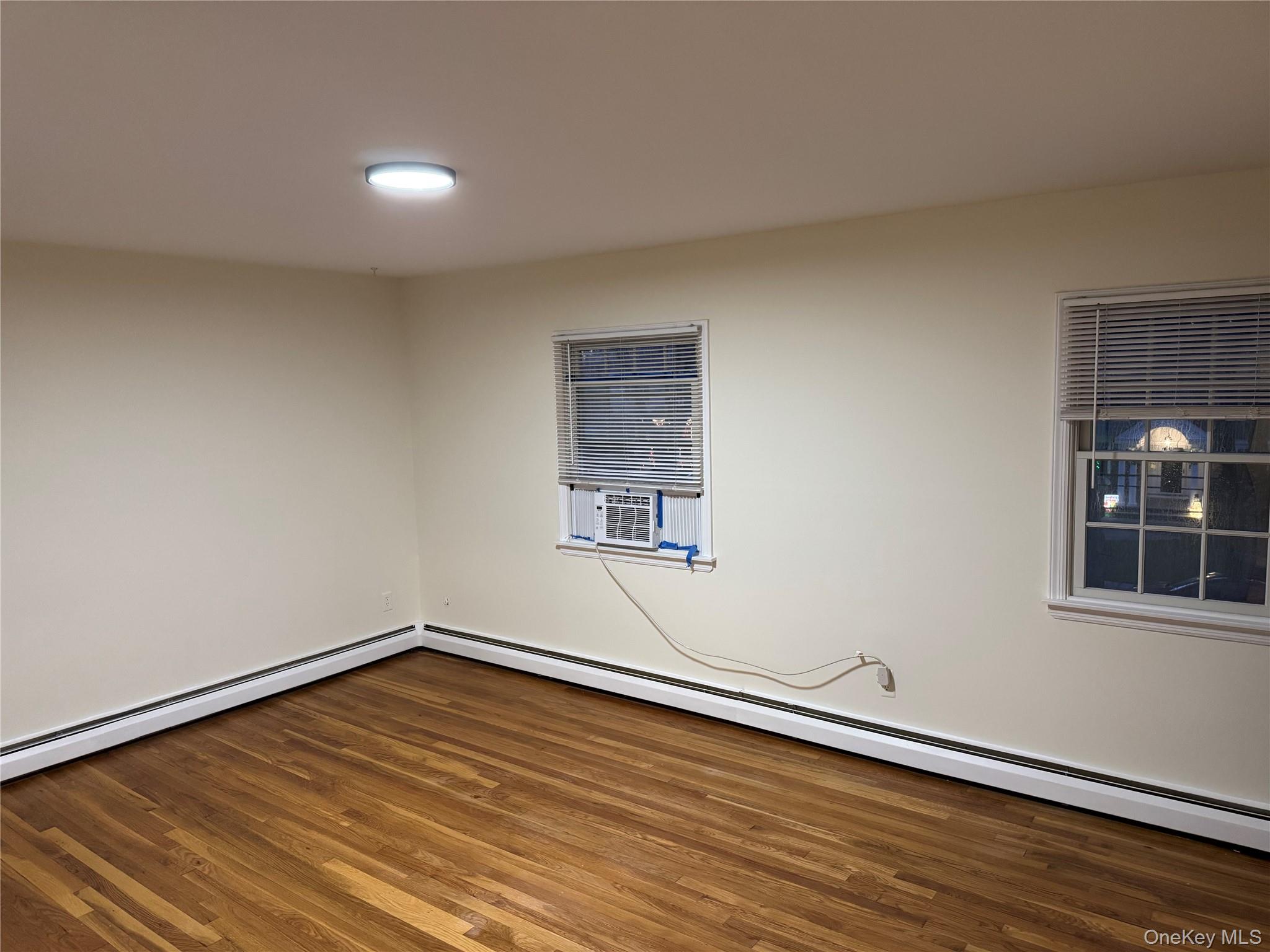 23 Jerome Road Syosset, NY 11791 - Photo 10 of 12 Empty room featuring baseboard heating, dark wood-type flooring, and cooling unit