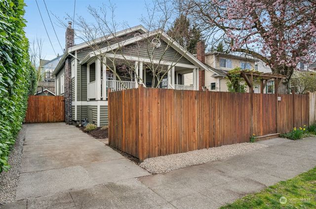 a view of small white house with a large tree and wooden fence