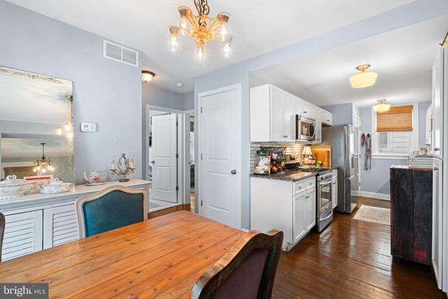 a kitchen with stainless steel appliances kitchen island granite countertop a refrigerator a stove top oven and a dining table with wooden floor