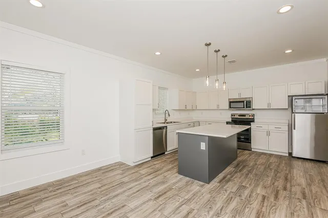 a kitchen with kitchen island wooden floors appliances and white cabinets