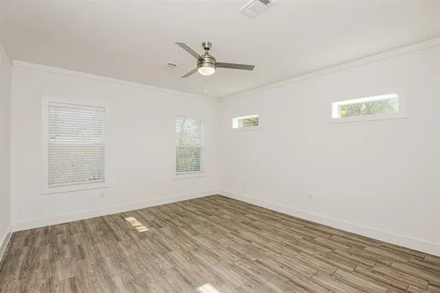 an empty room with wooden floor ceiling fan and windows