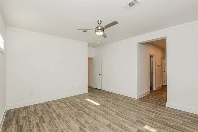 an empty room with wooden floor a ceiling fan and kitchen view