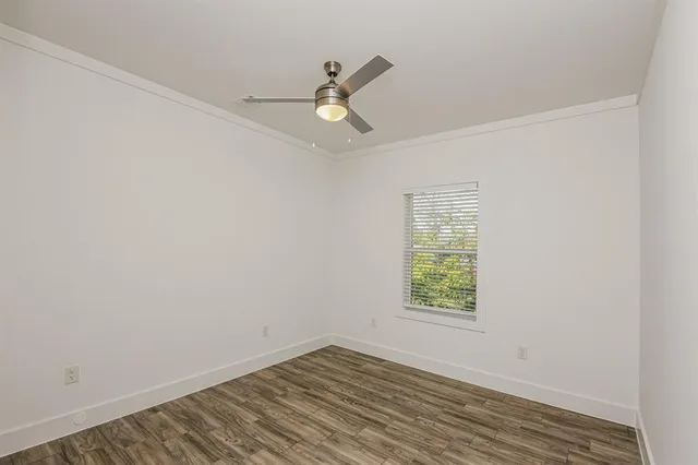 an empty room with wooden floor a ceiling fan and windows