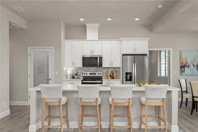 a dining area with stainless steel appliances kitchen island granite countertop a dining table chairs and a refrigerator