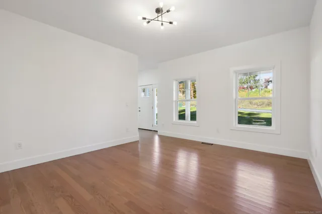 an empty room with wooden floor chandelier fan and windows