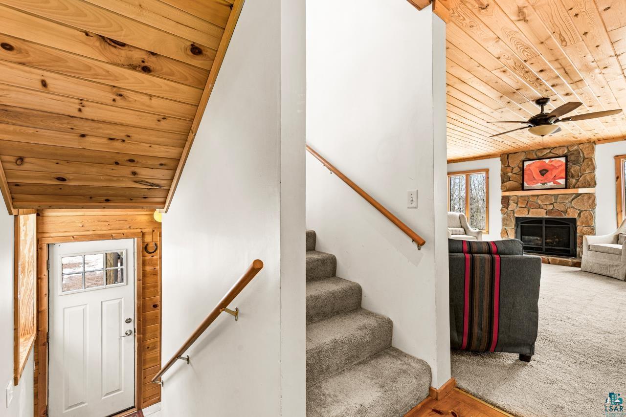 67 Snowshoe Trail Tofte, MN 55615 - Photo 27 of 42 Stairway featuring wooden ceiling, healthy amount of natural light, a stone fireplace, a ceiling fan, and carpet floors