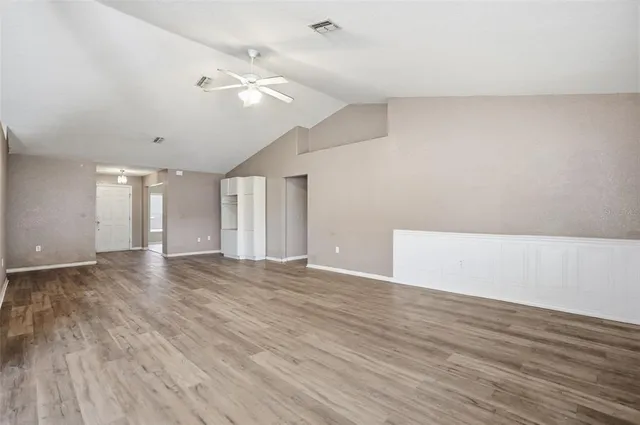 a view of an empty room with wooden floor and a ceiling fan