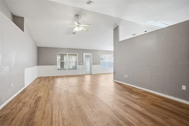 a view of an empty room with wooden floor and fan