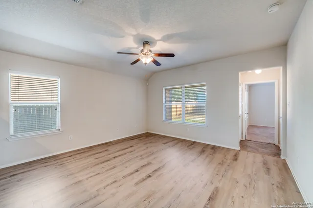 an empty room with wooden floor chandelier fan and windows