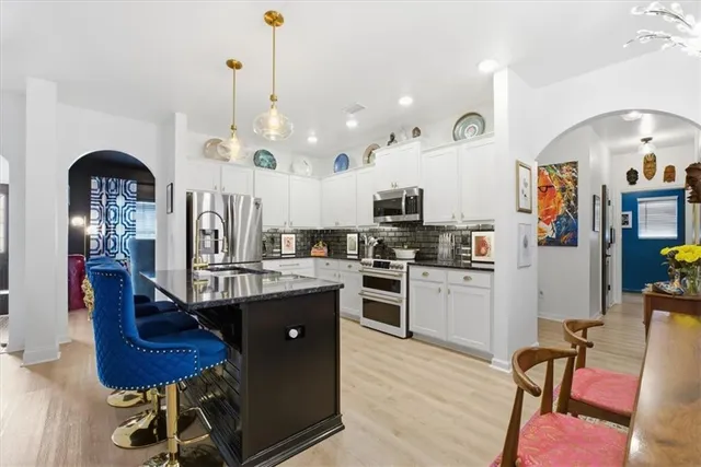 a kitchen with stainless steel appliances kitchen island granite countertop a refrigerator a stove top oven a sink dishwasher and white cabinets with wooden floor