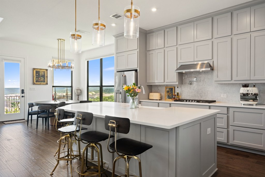 1221 Siena Sunset Road Leander, TX 78641 - Photo 18 of 39 Contemporary kitchen featuring a large central island with a white countertop, extensive grey cabinetry, stainless steel appliances, and wood-finish flooring