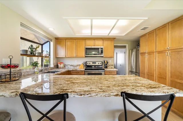 a kitchen with kitchen island granite countertop wooden cabinets a stove a sink a dining table and chairs