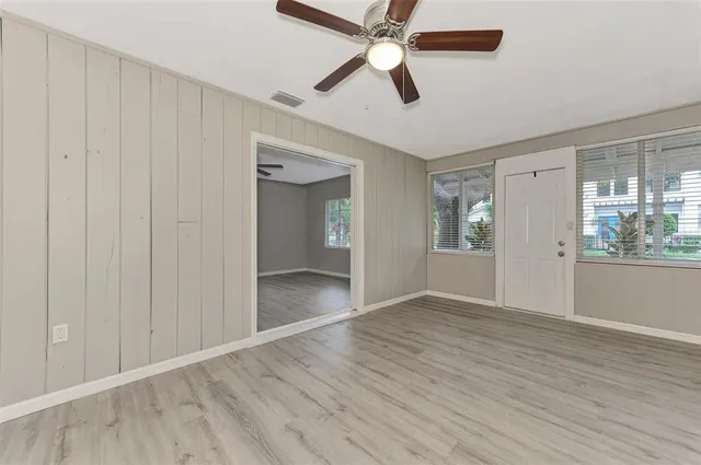 an empty room with wooden floor fan and windows