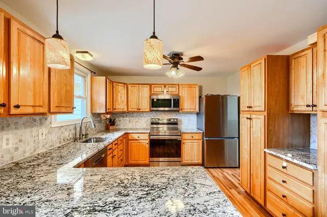 a kitchen with stainless steel appliances granite countertop a refrigerator a stove and a sink with wooden floor