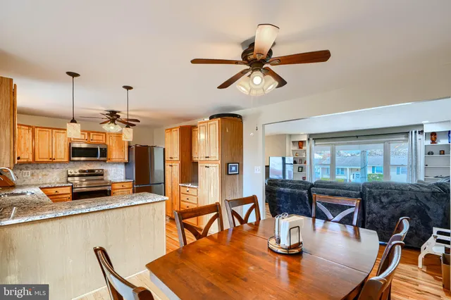 a kitchen with stainless steel appliances kitchen island granite countertop a stove a refrigerator a dining table and chairs with wooden floor