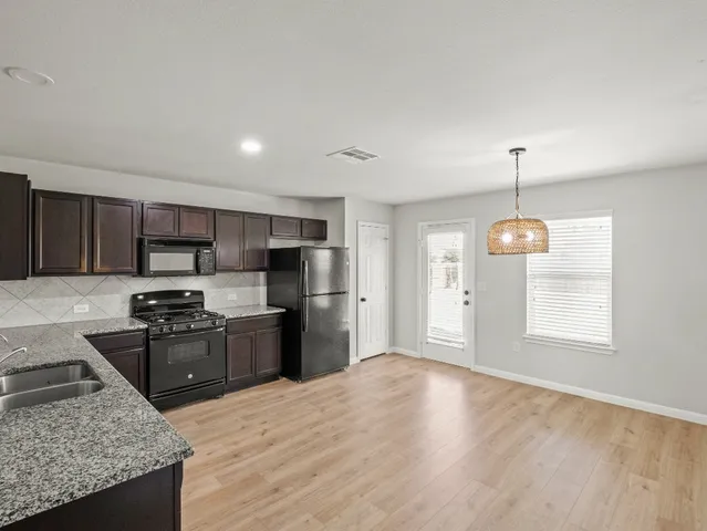 a kitchen with stainless steel appliances granite countertop a stove top oven a sink dishwasher a refrigerator and a dining table with wooden floor
