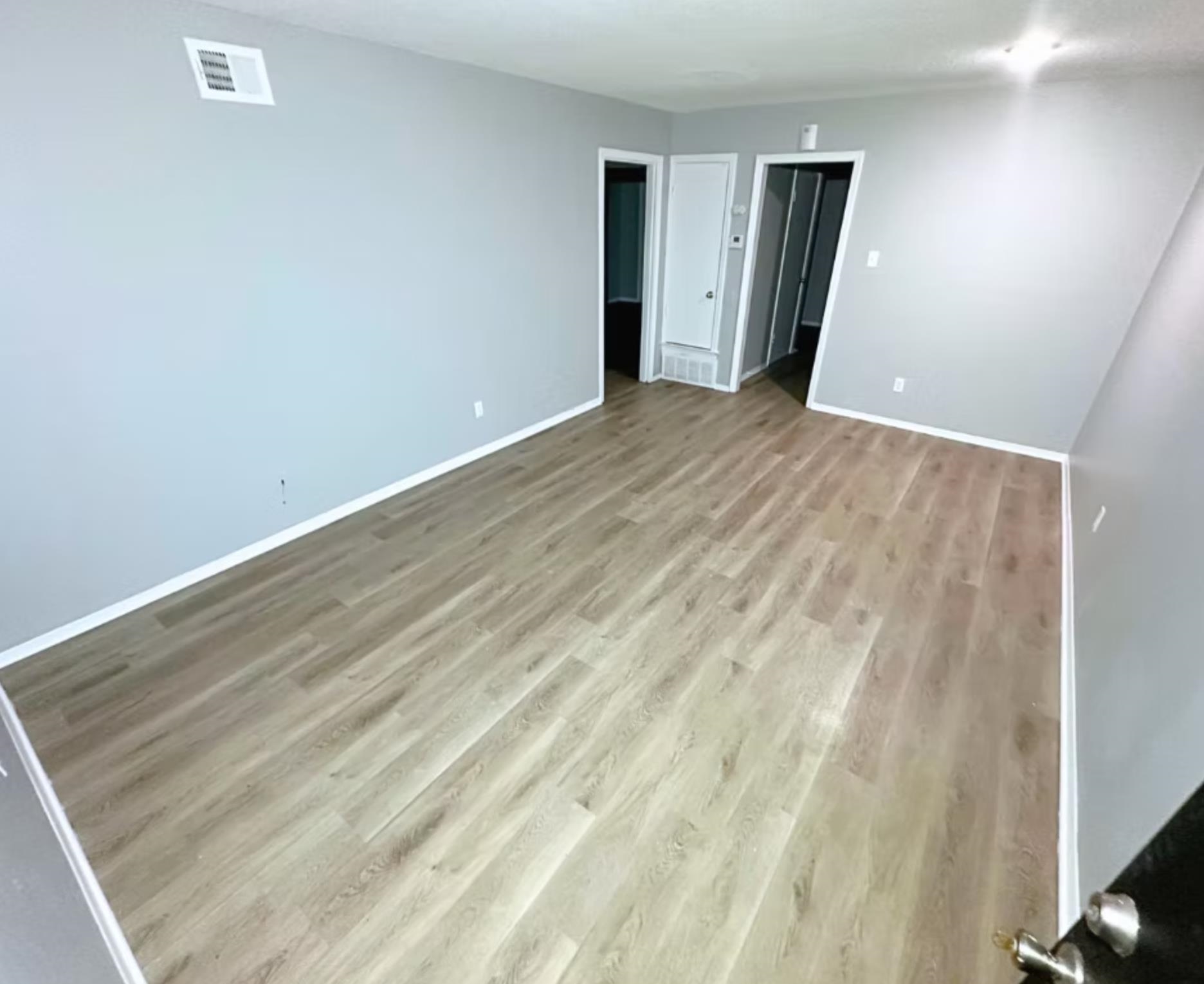 Empty room with wood finished floors, visible vents, and baseboards