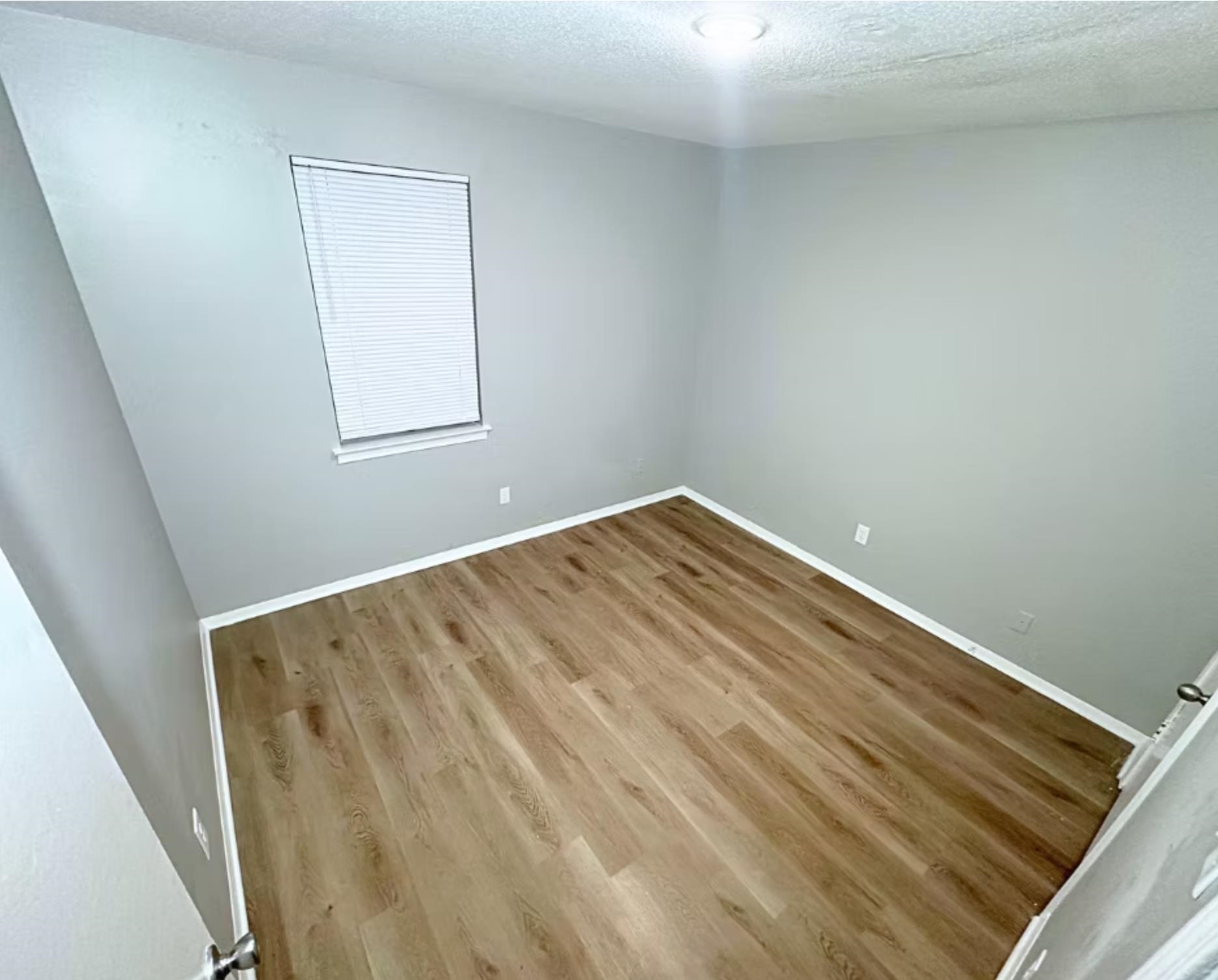 Empty room featuring a textured ceiling, baseboards, and wood finished floors