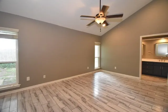 an empty room with wooden floor fan and windows