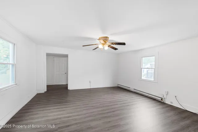 an empty room with wooden floor chandelier fan and windows