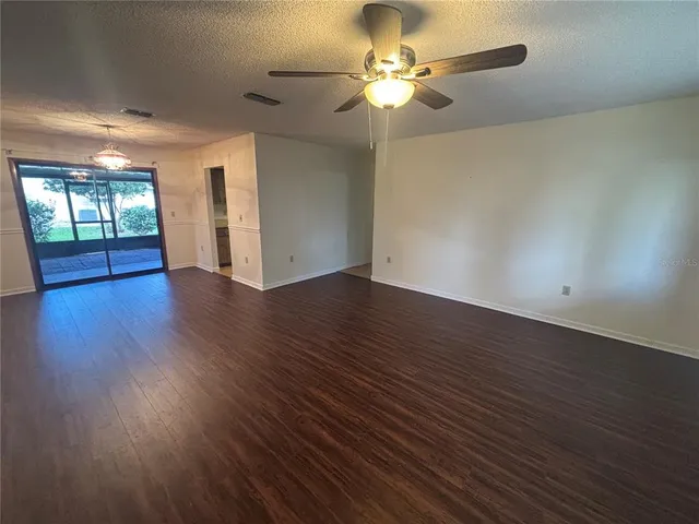a view of an empty room with wooden floor and a ceiling fan