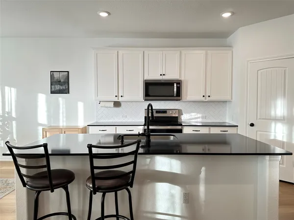 a kitchen with stainless steel appliances granite countertop a stove a sink a refrigerator and white cabinets with wooden floor