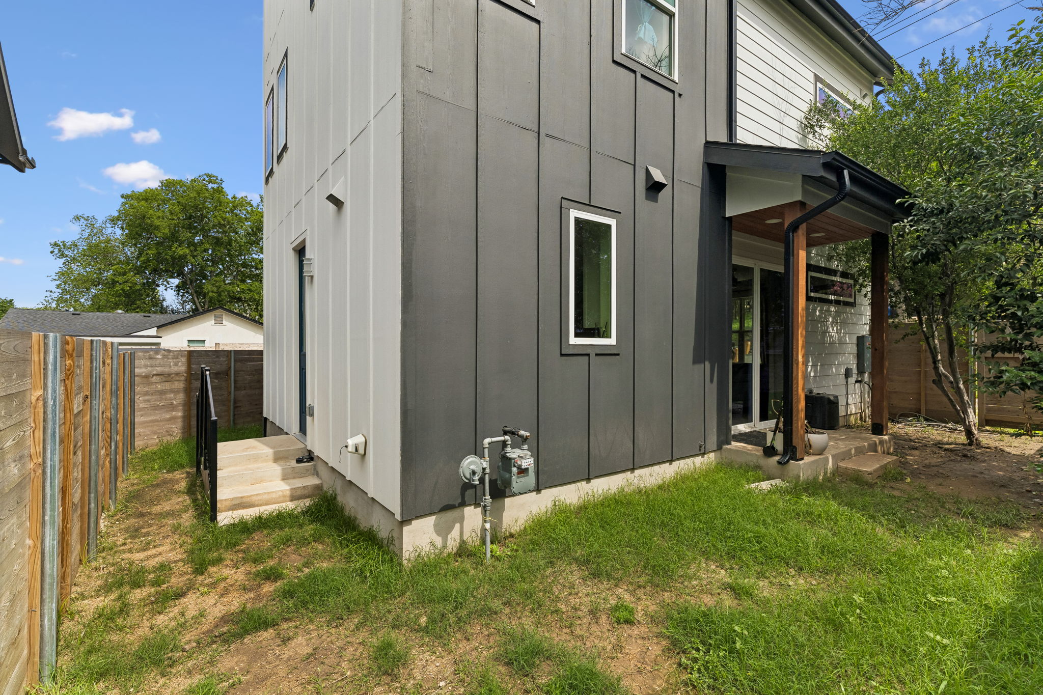 5305 Ledesma Road, Unit 1 Austin, TX 78721 - Photo 24 of 26 Exterior featuring vertical panel siding in a two-tone gray and white finish, a covered patio with wood support beams, and a wood privacy fence