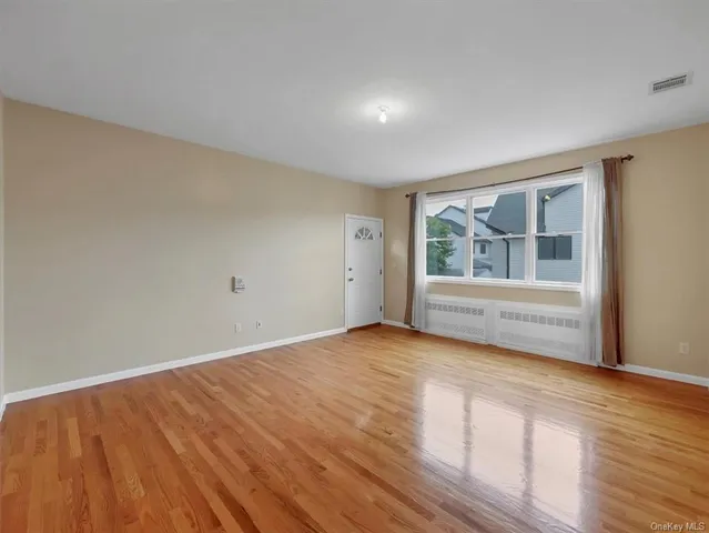 a view of an empty room with wooden floor and windows