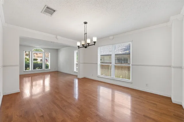 an empty room with wooden floor chandelier and windows