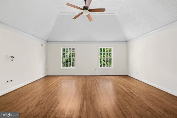 an empty room with wooden floor ceiling fan and windows