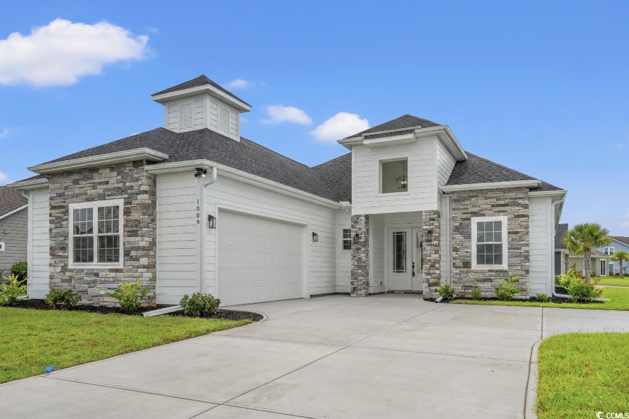 View of front of property featuring stone siding, driveway, a front lawn, and a shingled roof