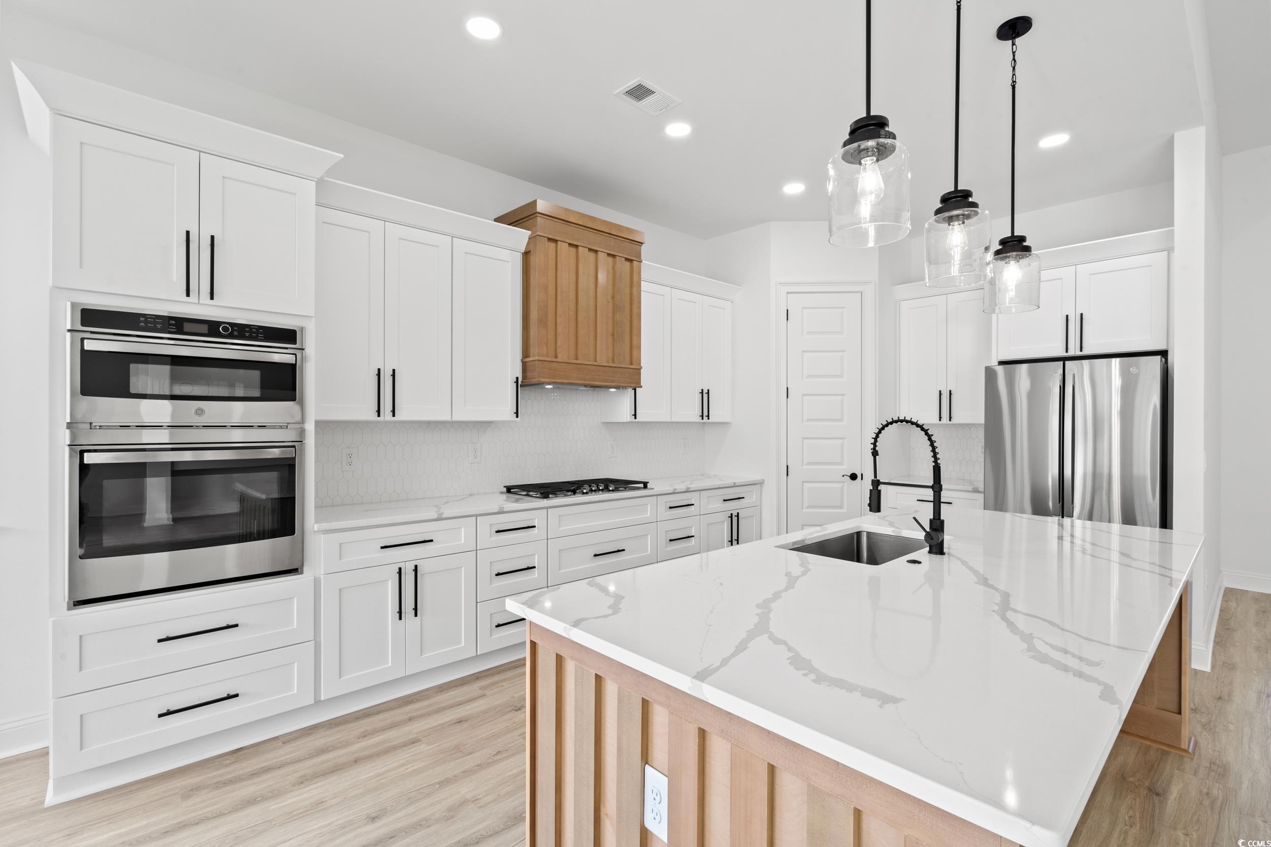 1009 Englemann Oak Drive Myrtle Beach, SC 29579 - Photo 6 of 38 Kitchen featuring backsplash, light stone counters, light wood-type flooring, appliances with stainless steel finishes, and white cabinets