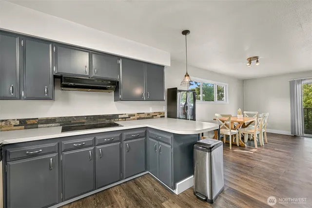 a kitchen with stainless steel appliances granite countertop a stove top oven a sink dishwasher a dining table and chairs with wooden floor