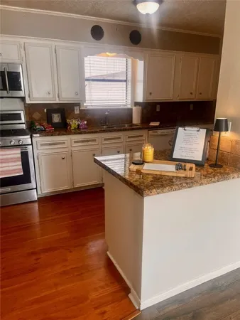a white kitchen with granite countertop a sink and dishwasher a stove top oven with wooden floor