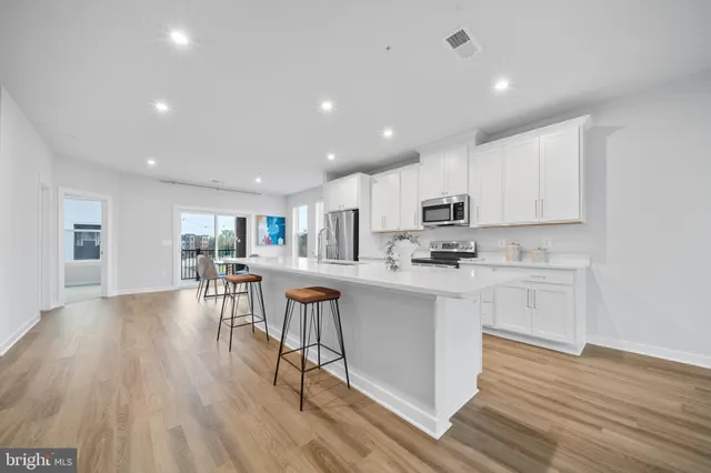 a kitchen with stainless steel appliances granite countertop a refrigerator a stove top oven a sink dishwasher and white cabinets with wooden floor
