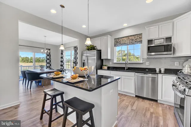 a kitchen with stainless steel appliances kitchen island granite countertop a stove a sink a microwave a dining table and chairs with wooden floor