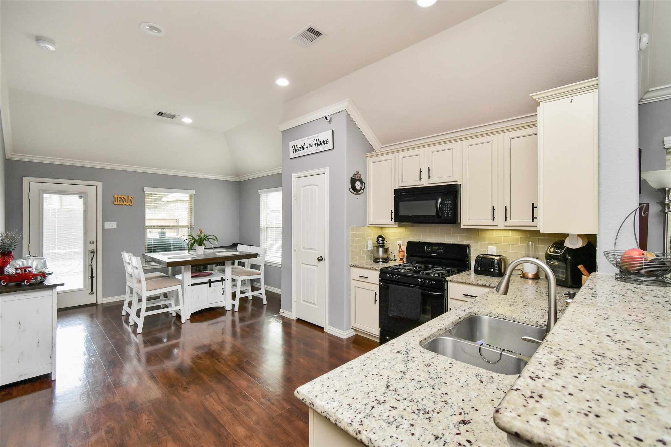 652 Maple Point Drive East Conroe, TX 77301 - Photo 9 of 35 This photo showcases a bright, open kitchen and dining area with elegant granite countertops, white cabinetry, and modern appliances. The space features hardwood floors, ample natural light, and a cozy dining nook by the window.