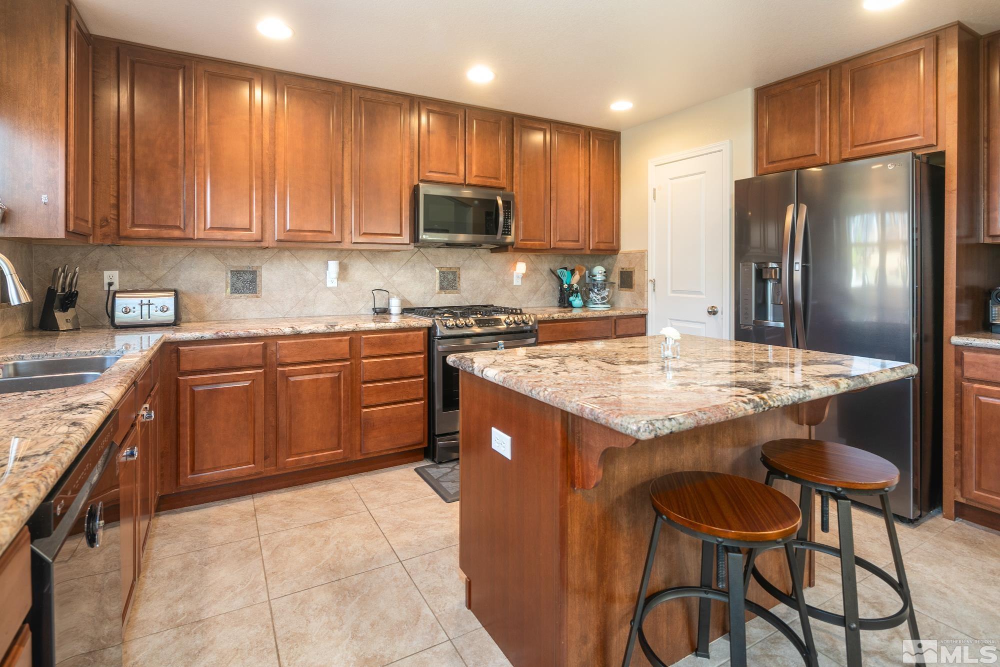 7665 Pebblestone Way Reno, NV 89523 - Photo 10 of 34 a kitchen with stainless steel appliances granite countertop a table chairs sink refrigerator and microwave