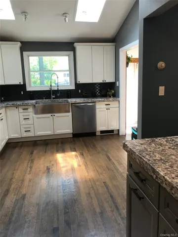a kitchen with granite countertop a stove a sink and white cabinets with wooden floor